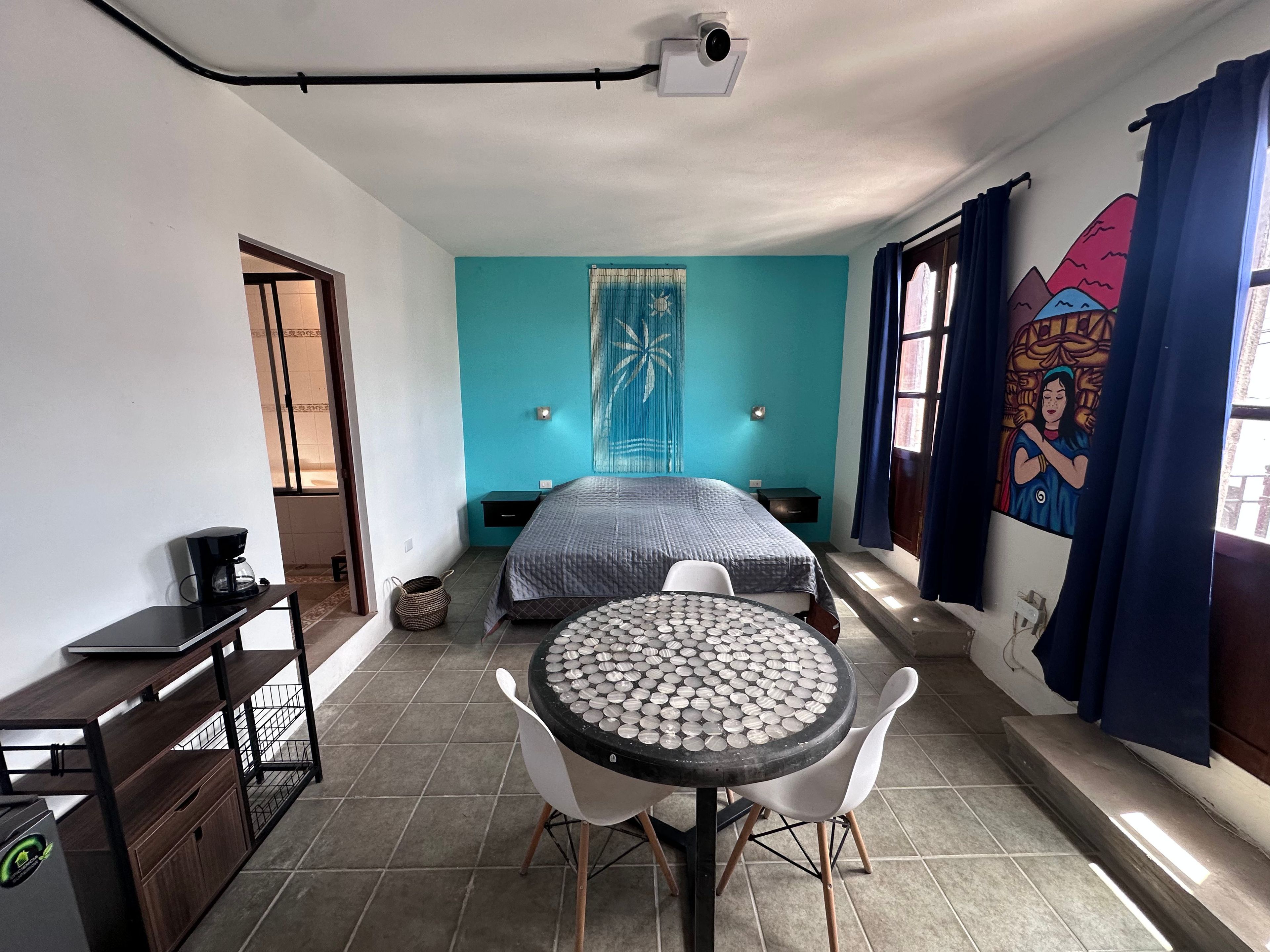 A room with a bed, a table with a unique patterned tabletop, a coffee maker, and a wall-mounted projector.