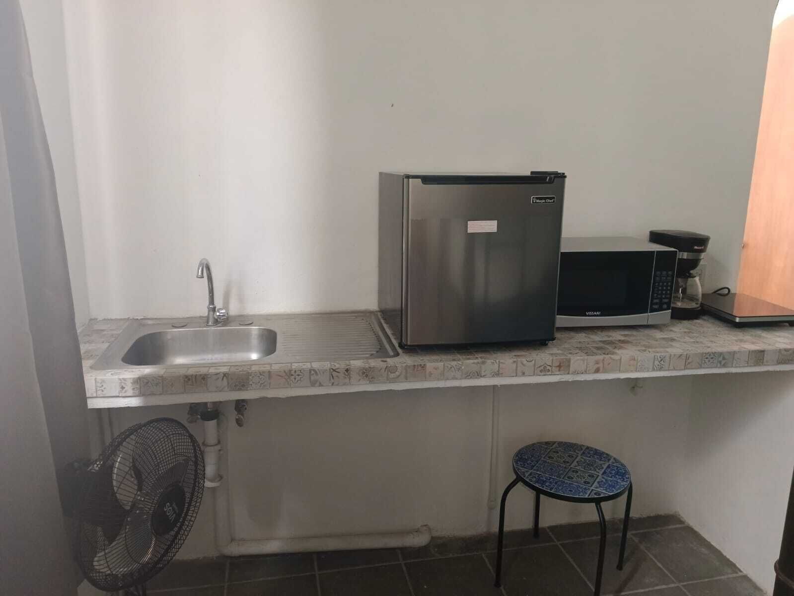 Una kitchenette compacta con un lavamanos de acero inoxidable, un refrigerador, un microondas y una pequeña mesa.