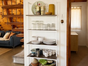 A white shelving unit with glassware, plates, and mugs.