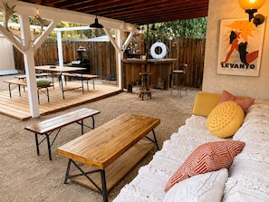 An outdoor patio area with wooden tables and benches, a barbecue grill, and a bar area with stools.
