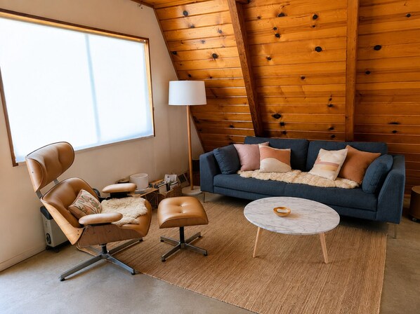 A modern living room with a leather chair, a blue sofa, a round coffee table, and a lamp.