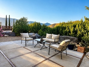 An outdoor patio with a seating arrangement, a table, and a view of a mountainous landscape.