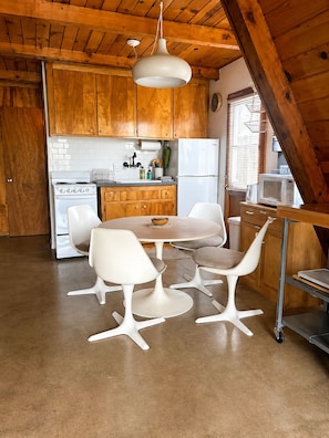 A kitchen with wooden cabinets, a stove, a refrigerator, a microwave, and a dining table with chairs.