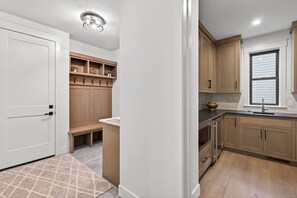 A modern kitchen with wooden cabinets, a built-in bench, and a window with blinds. - Brand New Home in Downtown Wayzata! (Wayzata)