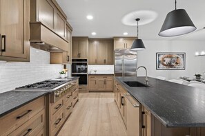 Eine moderne Küche mit Holzausstattung, einer schwarzen Arbeitsplatte, Edelstahlgeräten und einer Pendelleuchte.