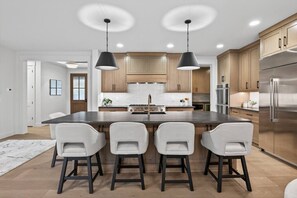 A modern kitchen with a central island, bar stools, pendant lighting, and stainless steel appliances.