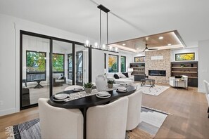 Ein modernes Wohnzimmer mit Essbereich, großen Fenstern, einem Kamin und einer Wand mit Steinverkleidung.