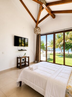 A bedroom with a large bed, a television, a nightstand, and a view of the beach.