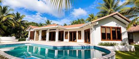 A modern house with a swimming pool, surrounded by palm trees and a clear sky.