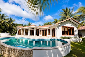 Una casa moderna con piscina, rodeada de palmeras y un cielo despejado.