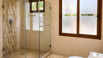 A modern bathroom with a glass-enclosed shower, a toilet, and a window with frosted glass.