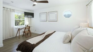 Ein Schlafzimmer mit einem Bett, einem Schreibtisch, einem Stuhl, einem Deckenventilator und einem Fenster mit Vorhängen.
