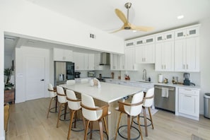 A modern kitchen with white cabinetry, a central island with bar stools, and a ceiling fan. - 5bd Home w/ Pool, Home Theater, Kayak & Golf cart (Indian Rocks Beach)