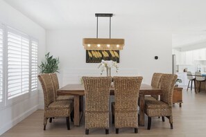 A dining area with a wooden table and wicker chairs, a pendant light, and a wall-mounted painting. - 5bd Home w/ Pool, Home Theater, Kayak & Golf cart (Indian Rocks Beach)
