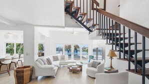 Ein großzügiger Wohnbereich mit Treppe, weißen Sofas, einem Couchtisch und Blick ins Freie.