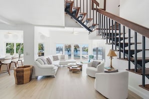 Ein großzügiger Wohnbereich mit Treppe, weißen Sofas, einem Couchtisch und Blick ins Freie.