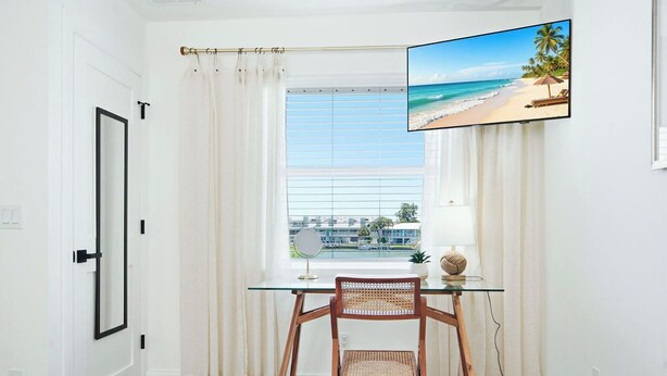 Ein Zimmer mit Schreibtisch, Stuhl und einem Fenster mit Blick auf einen Strand.