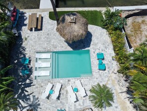 An aerial view of a swimming pool area with lounge chairs and a thatched umbrella. - 5bd Home w/ Pool, Home Theater, Kayak & Golf cart (Indian Rocks Beach)