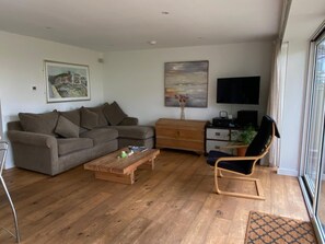 Una sala de estar con un sofá modular, una mesa de centro de madera, un televisor y una silla.