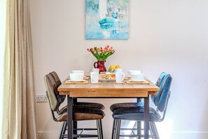 Una mesa de comedor con sillas, un jarrón con flores y un cuadro en la pared.