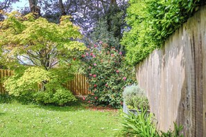 A garden with a wooden fence, various shrubs, and a tree with pink flowers. - The Garden Room - luxury hideaway, Bantham, Devon (Bantham)