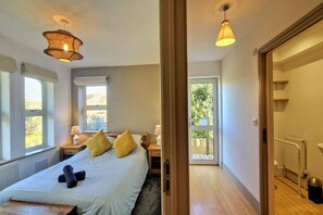 A bedroom with a bed, bedside tables, a window, and a door leading to a balcony. - Butter Bay apartment, Bantham, Devon (Bantham)