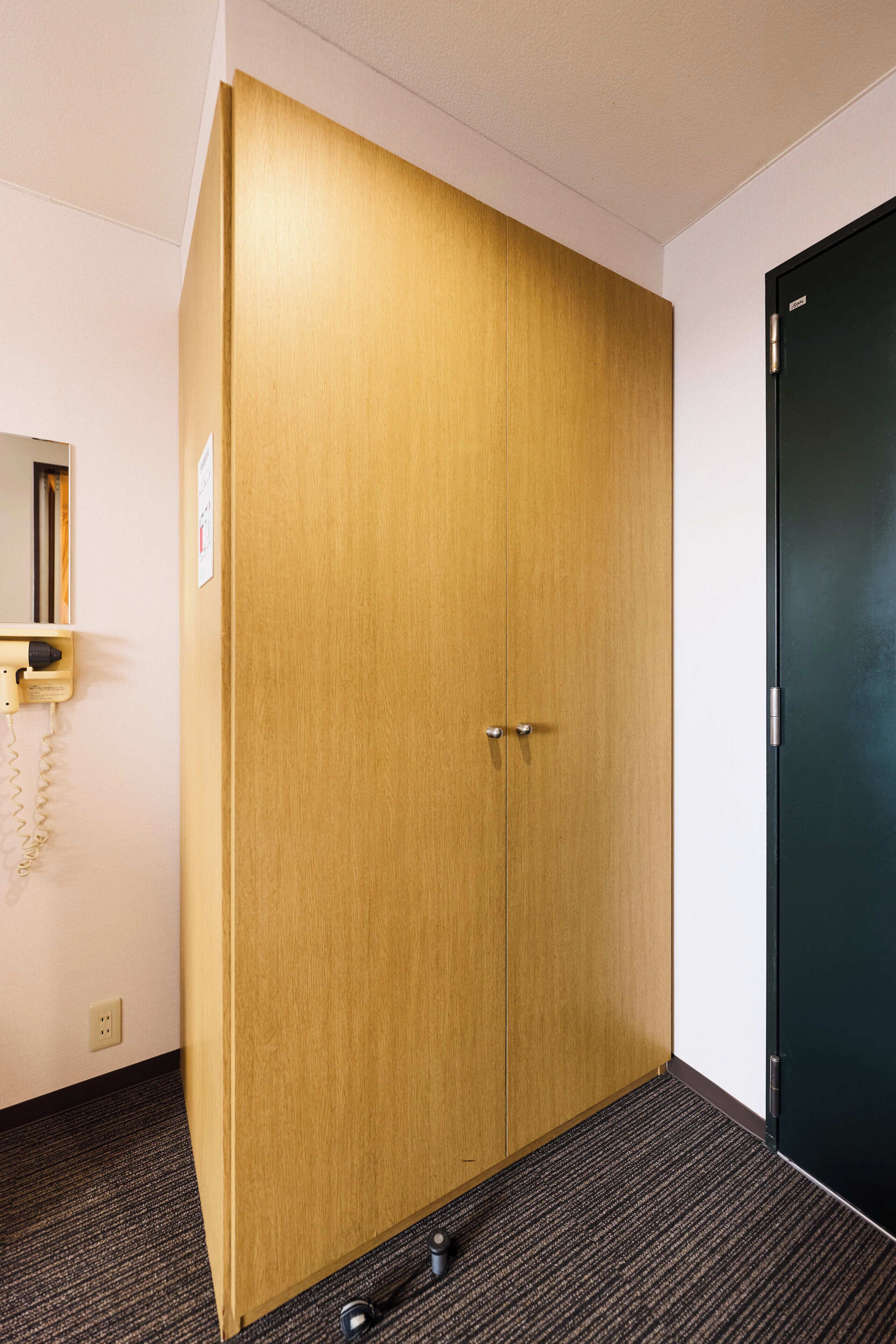 A room with a large wooden wardrobe, a black door, a telephone, and a carpeted floor.