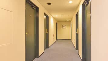 A hotel hallway with doors on both sides, carpeted floor, and a ceiling with recessed lighting.