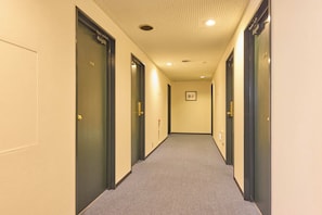 Corredor de hotel com portas em ambos os lados, piso coberto de carpete e teto com iluminação embutida.