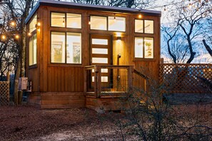 A wooden cabin with large windows, a front door, and a small porch. - Selena, Cozy Tiny House in Gladheart Fredericksburg, w/Hot Tub & Firepit (Fredericksburg)