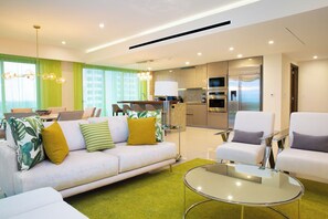 A modern living room with a sofa, armchairs, a glass coffee table, and a kitchen area in the background. - Garza Blanca Luxurious Oceanfront 3-Bedroom with Expansive Balcony and Jacuzzi (Cancún)