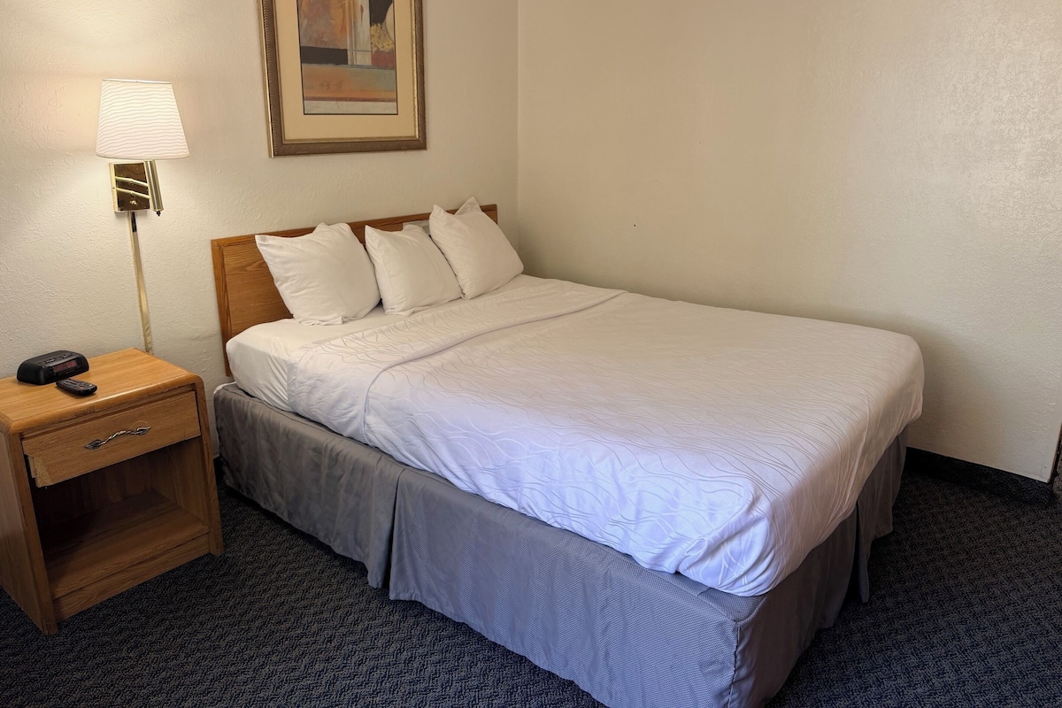 A hotel room with a bed, a nightstand with a lamp, and a painting on the wall.