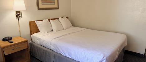 A hotel room with a bed, a nightstand with a lamp, and a painting on the wall.