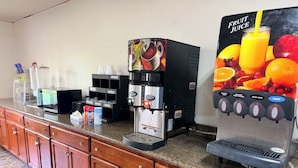 Una estación de café con una máquina de café, un dispensador de jugo y una estación de condimentos.