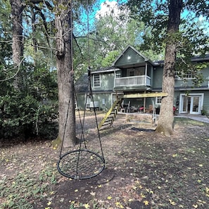 A two-story house with a porch and a swing set. - Large Farm House Theme Home on Wooded Lot and Still Close to Everything (Spring)