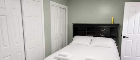 A bedroom with a bed, two white doors, a dark headboard, and a ceiling fan.