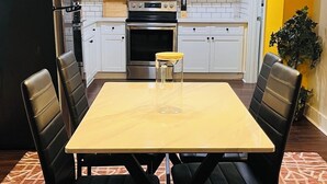 Una cocina moderna con armarios blancos, un refrigerador de acero inoxidable, un horno y un microondas. Hay una mesa de comedor con cuatro sillas.