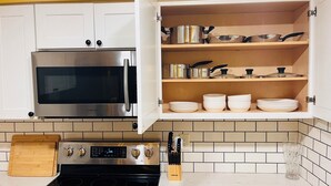 Una cocina con microondas de acero inoxidable, estufa a gas y un armario con utensilios de cocina y platos.
