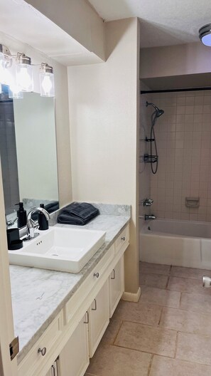 A bathroom with a white sink, mirror, and vanity, a shower with a handheld showerhead, and a bathtub.
