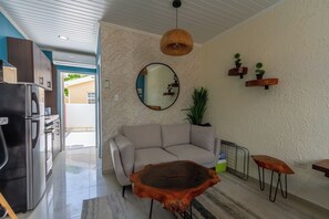 A modern living room with a sofa, a coffee table, a hanging light fixture, and a mirror on the wall. - Aruba Vibe Apartments 7 | Charming Studio Near the Beaches & Downtown (Oranjestad)