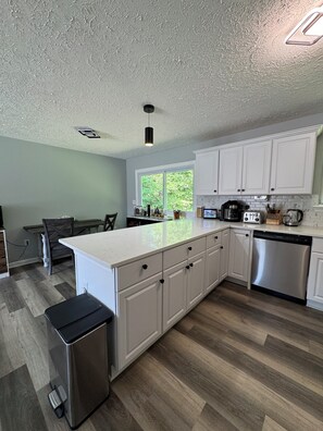 A modern kitchen with white cabinetry, a stainless steel dishwasher, and a large island with a black trash bin. - 3-bedrooms in quaint Dumfries with AC (Dumfries)