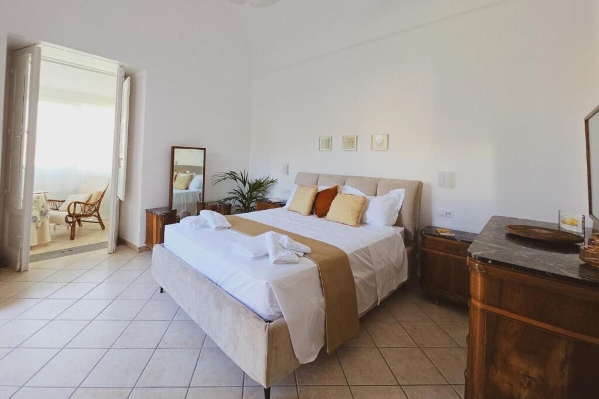 Ein Hotelzimmer mit Bett, Schreibtisch, Stuhl, Pflanze und Blick ins Freie.