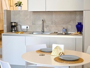 Eine kleine Küche mit Spüle, Kaffeemaschine und einer Vase auf der Arbeitsplatte.