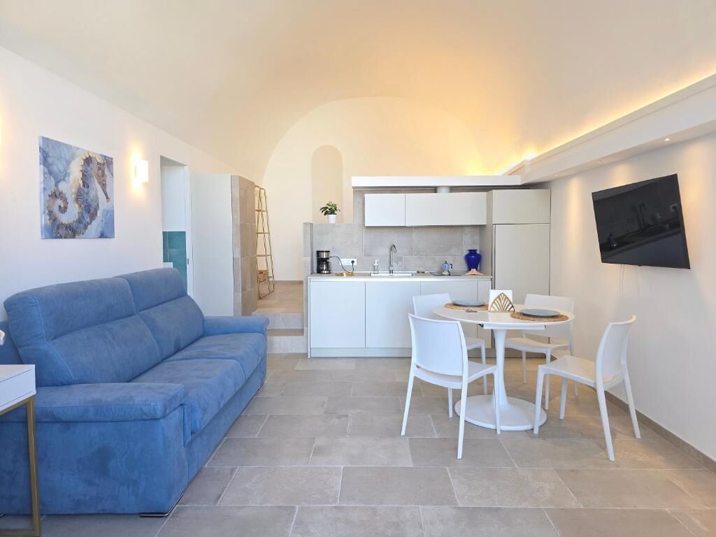 Una cocina moderna con armarios blancos, una zona de comedor con sillas blancas y un sofá azul.