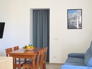 Ein Zimmer mit Esstisch, Obstschale, Sofa und einem gerahmten Bild an der Wand.