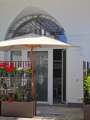 Ein Gebäudeeingang mit überdachter Terrasse, Glastür und Metalltreppe.