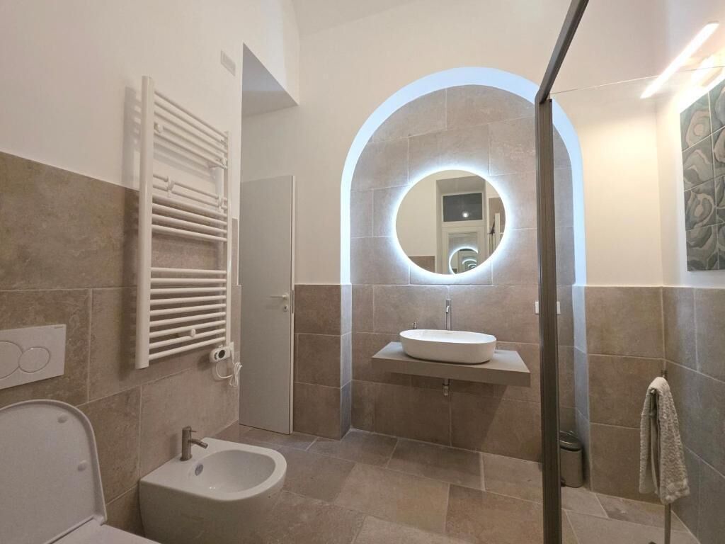 Un baño moderno con una bañera independiente, un espejo redondo con iluminación integrada y un tocador con lavamanos.