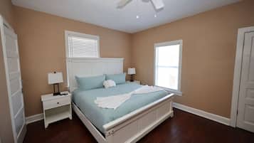 A bedroom with a bed, two bedside tables, a ceiling fan, and two windows with blinds.