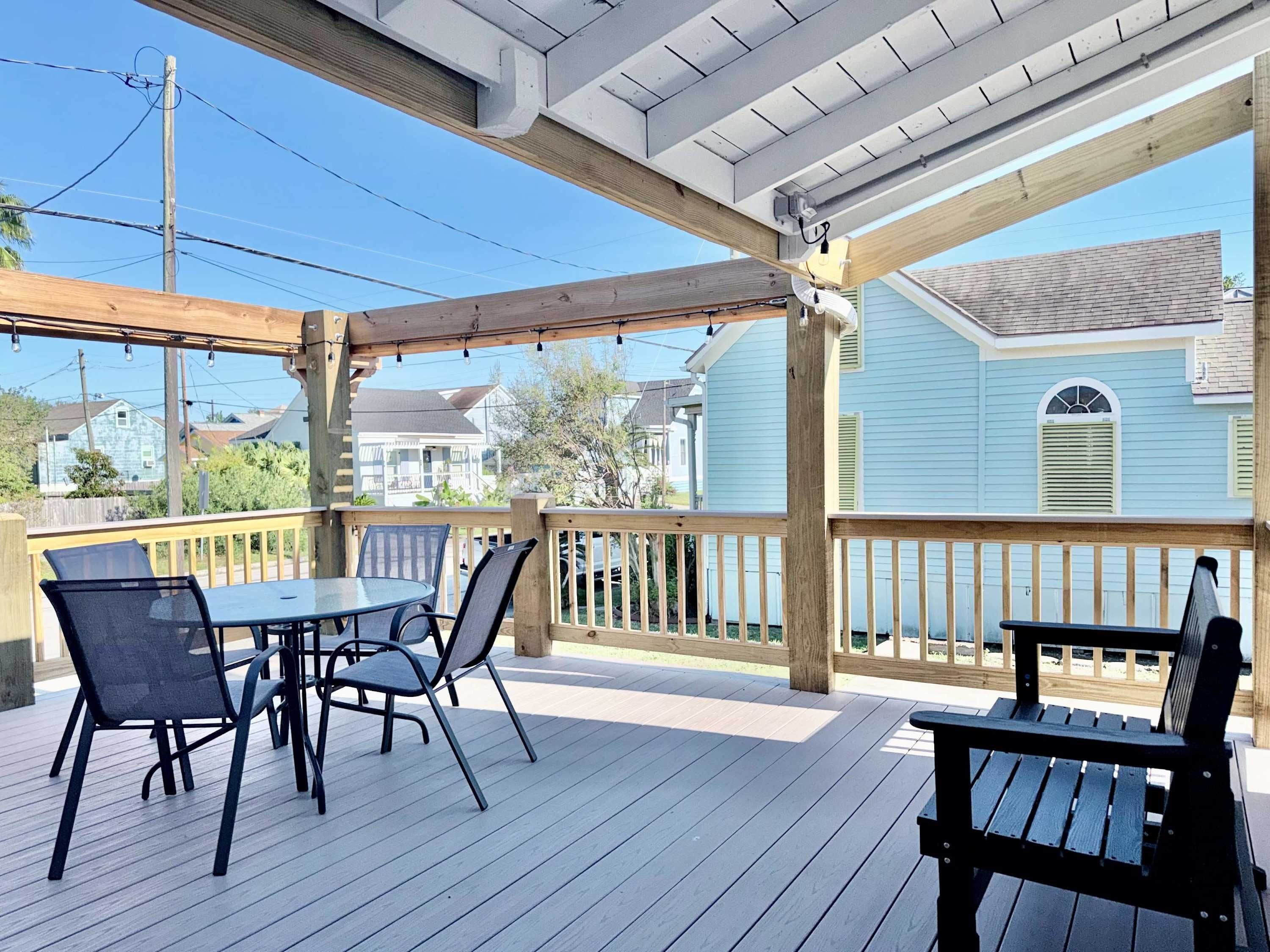 Eine überdachte Terrasse im Freien mit Tisch und Stühlen, Holzgeländern und Blick auf benachbarte Häuser.