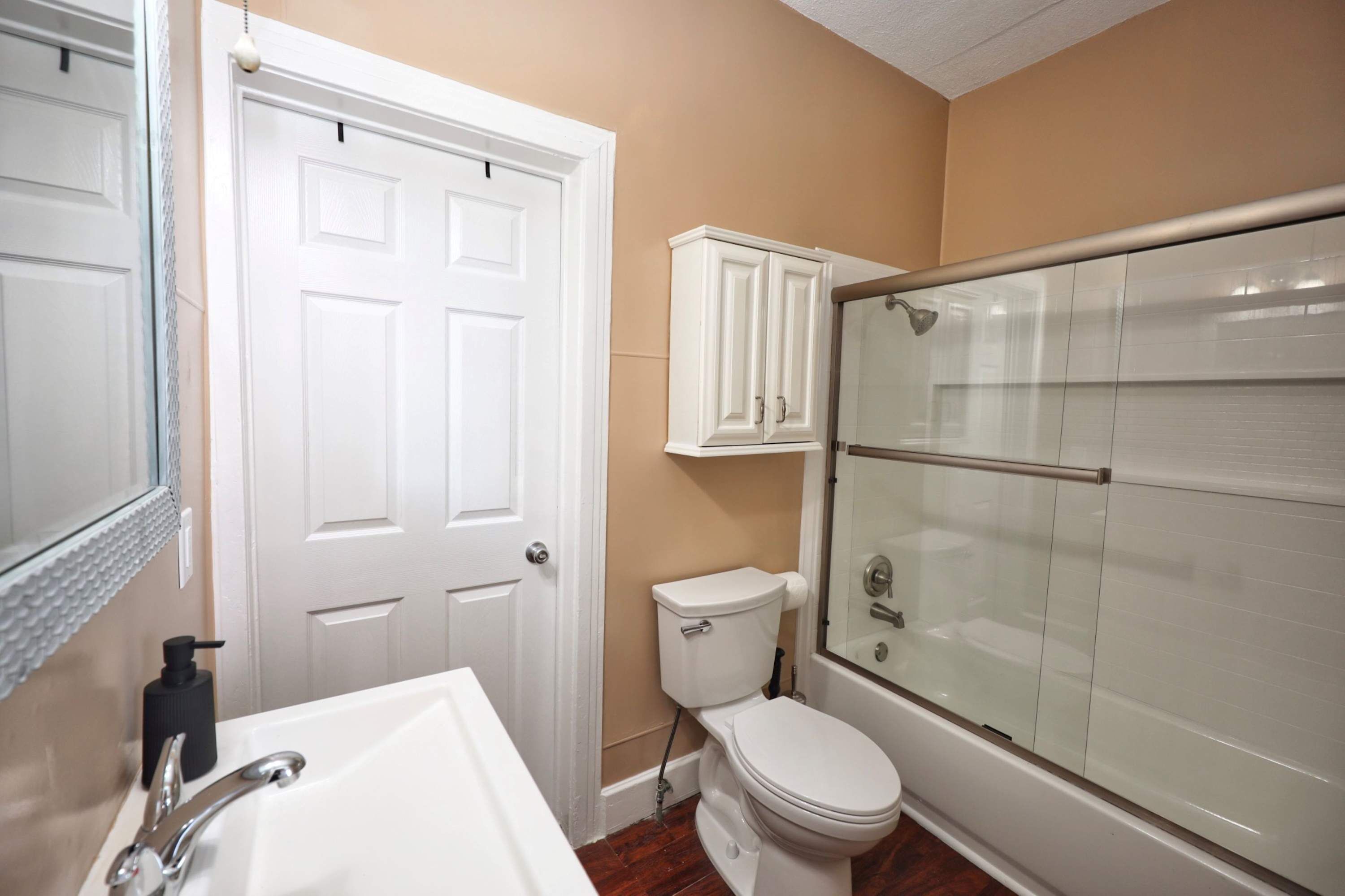 Een badkamer met een wit toilet, een witte wastafel, een douchecabine en een kast.